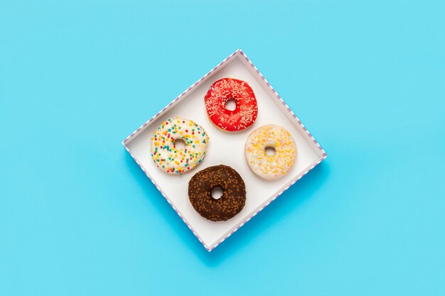 Leckere Donuts in einer Schachtel auf einem blauen Feld. Konzept von Süßigkeiten, Bäckerei, Gebäck, Café.