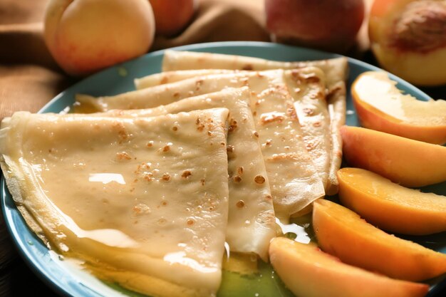 Leckere dünne Pfannkuchen mit Pfirsichen auf Plattennahaufnahme