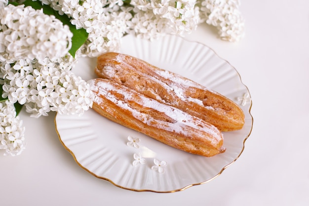 Leckere Eclairs auf Teller mit Blumenstrauß