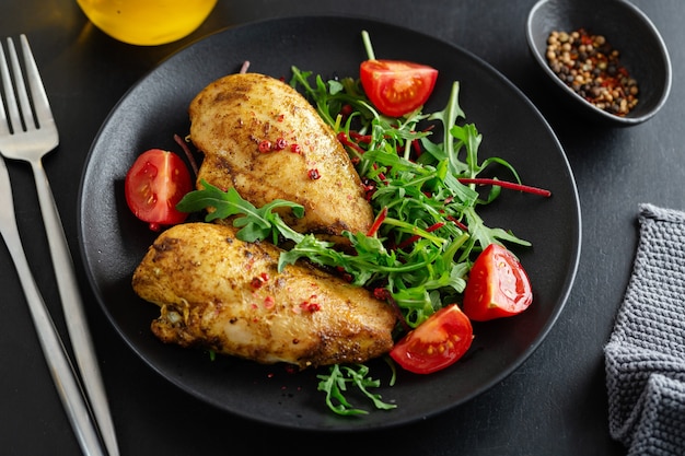 Leckere gegrillte Hühnerbrust mit Gemüse und Salat auf dunklem Tisch serviert.