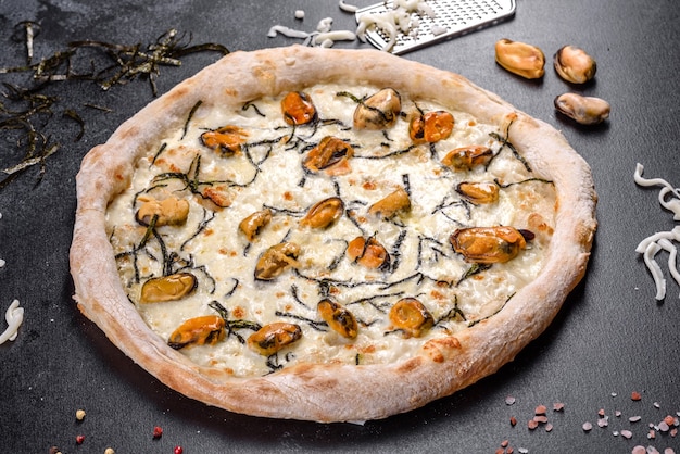 Leckere geschnittene Pizza mit Meeresfrüchten und Tomaten auf schwarzem Hintergrund. Mediterrane Küche