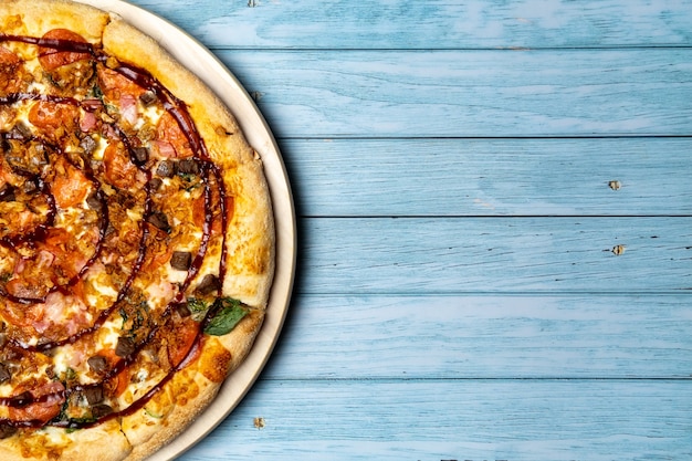 Leckere große Pizza mit Speck und Spinat auf blauem Holzhintergrund.