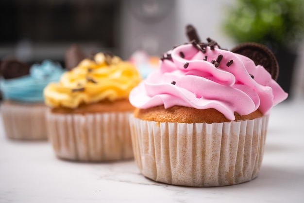 Leckere hausgemachte Cupcakes mit bunter Sahne und Topping mit Süßigkeiten und Schokoladenkeksen