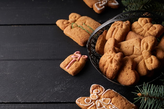 Leckere hausgemachte Kekse mit Zuckerguss auf dunklem Tisch mit Tannenzweig. Weihnachts- und Winterkonzept Nahaufnahme