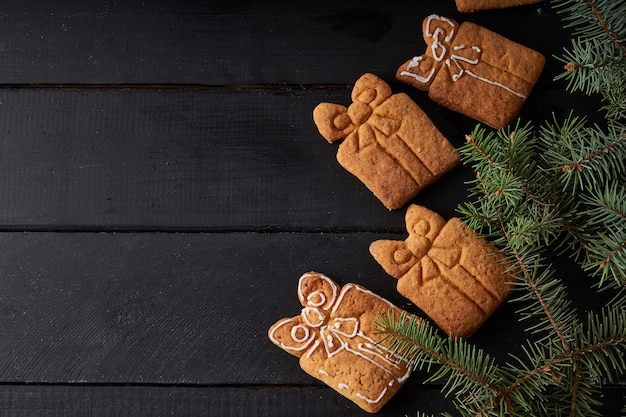 Leckere hausgemachte Kekse mit Zuckerguss auf dunklem Tisch mit Tannenzweig. Weihnachts- und Winterkonzept Nahaufnahme