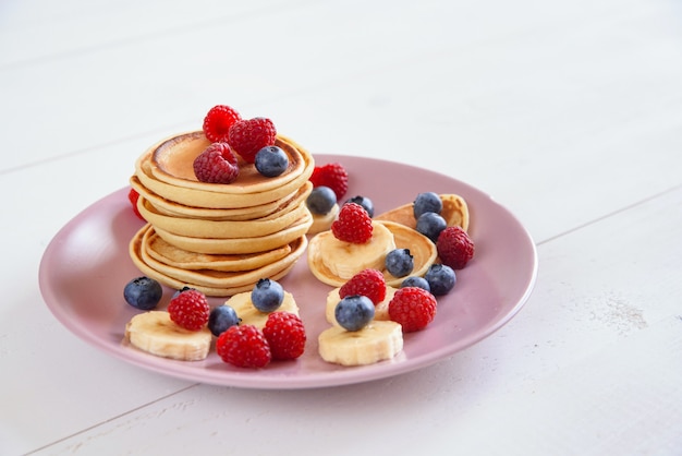 Leckere hausgemachte Pfannkuchen mit frischen Beeren in einem violetten Teller Ein leckeres und gesundes Frühstück mit Pfannkuchen mit Himbeeren, Blaubeeren und Bananen.