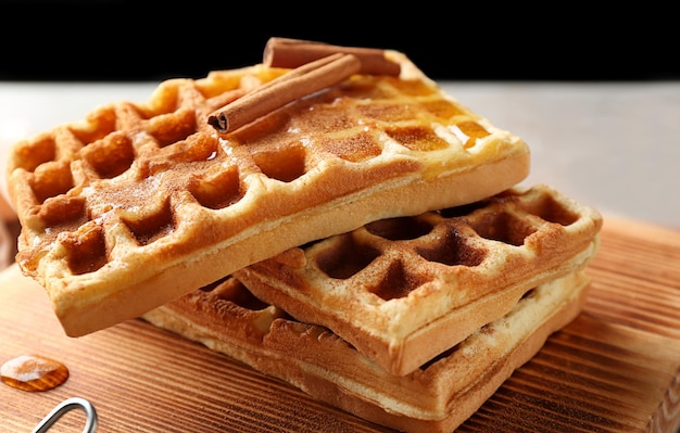 Leckere hausgemachte Waffeln mit Honig und Zimtstangen auf Holzbrett