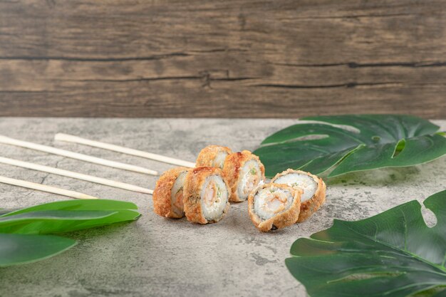Leckere heiße sushi-rollen und essstäbchen auf steinoberfläche.