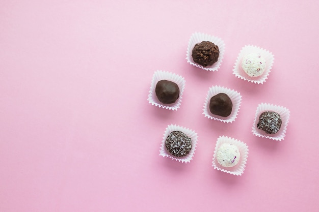 Leckere kugelförmige Pralinen verpackt in kleinen Papierkörben auf rosa Hintergrund. Romantisches Dessert zum Valentinstag. Köstlich süß. Minimaler Stil. Flache Lage, Draufsicht mit Kopie scape.