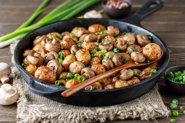 Leckere Ofenkartoffeln in einer Gusseisenpfanne mit Champignons und Frühlingszwiebeln