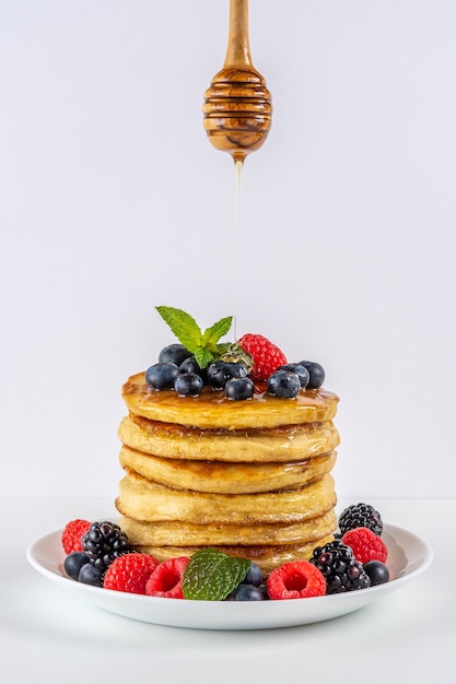 Leckere Pfannkuchen mit frischen Beeren und tropfendem Honig auf weißem Tisch