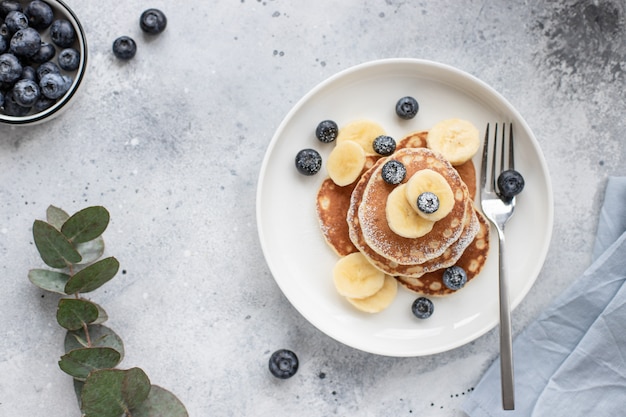 Leckere Pfannkuchen mit frischen Blaubeeren, Banane und Puderzucker auf einem grauen Betonhintergrund. horizontales Bild, Draufsicht, Platz für Text