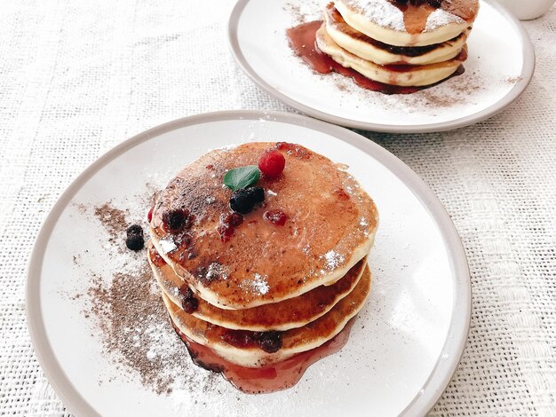 Leckere Pfannkuchen mit Sirup und Beeren auf stilvollem Teller auf rustikalem Tisch Leckeres hausgemachtes Frühstück Stapel Pfannkuchen mit Marmelade Nahaufnahme perfektes Rezept Telefonfoto