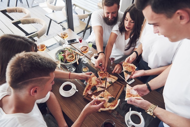 Leckere Pizza auf dem Tisch, mit einer Gruppe junger lächelnder Leute, die sich in der Kneipe ausruhen