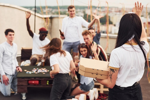 Leckere Pizza Eine Gruppe junger Leute in lässiger Kleidung feiern tagsüber gemeinsam auf dem Dach