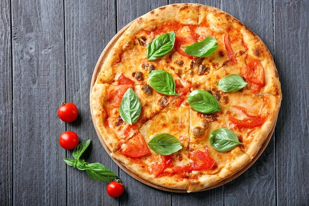 Leckere Pizza mit Kirschtomaten und frischem Basilikum auf Küchentisch