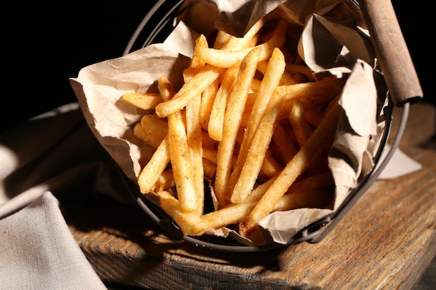 Leckere Pommes Frites im Metallkorb auf Holztisch mit dunklem Licht