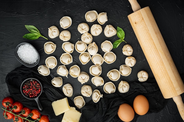 Leckere rohe Tortellini mit Mehl und Basilikum, auf schwarzem Hintergrund, Draufsicht flach gelegt