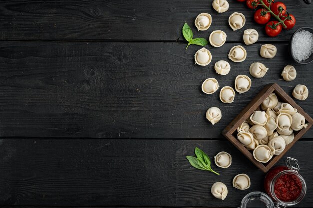 Leckere rohe Tortellini mit Mehl und Basilikum auf schwarzem Holztisch