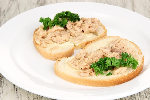 Leckere Sandwiches mit Thunfisch und Dorschlebersardinen auf weißem Teller auf Holzhintergrund