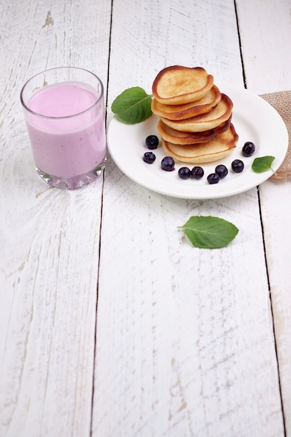 Leckere schöne Pfannkuchen mit Blaubeeren und Blaubeerjoghurt auf einem hellen Holztisch mit Minzblättern.