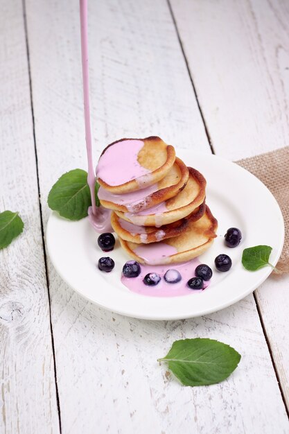 Leckere schöne Pfannkuchen mit Blaubeeren und Blaubeerjoghurt auf einem hellen Holztisch mit Minzblättern.