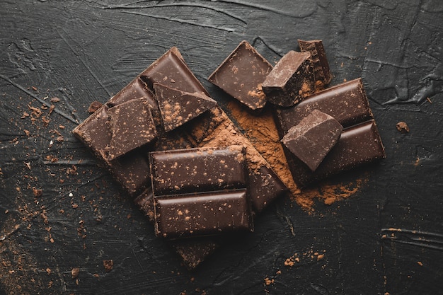 Leckere Schokolade und Pulver auf schwarzem Hintergrund