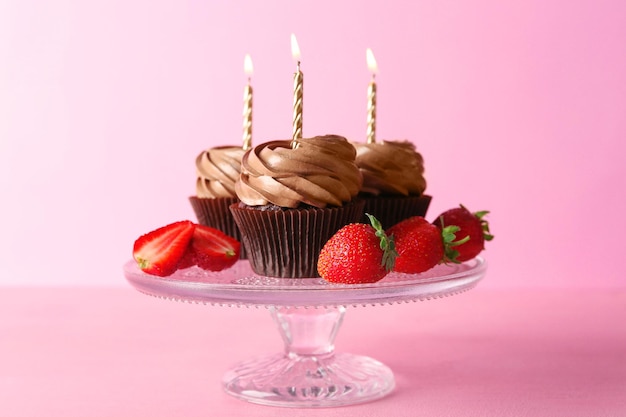 Leckere Schokoladen-Cupcakes mit Beeren auf rosa Hintergrund