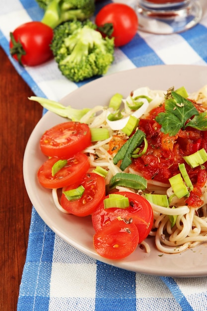 Leckere Spaghetti mit Soße und Gemüse auf Teller auf Holztisch in der Nähe