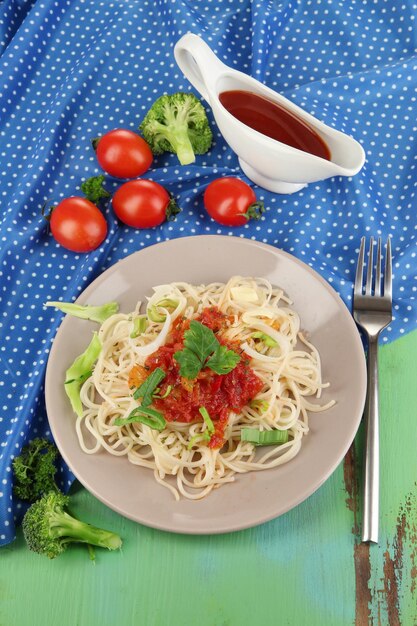 Leckere Spaghetti mit Soße und Gemüse auf Teller auf Holztisch in der Nähe