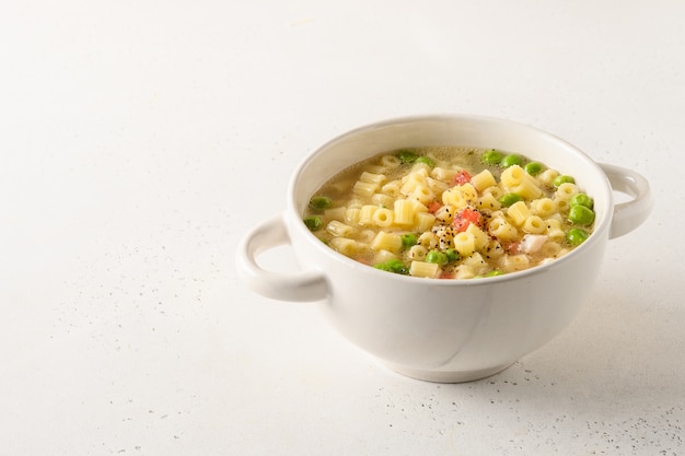 Leckere Suppe mit Ditalini-Nudeln, Erbsen, Tomaten, Schinken auf weißem Tisch.