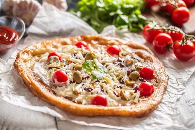 Leckere und knusprige Langos, perfekt serviert mit ganzen Kirschtomaten, geriebenem Käse, Bohnen und grünen griechischen Oliven.