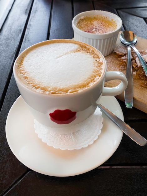 Leckere weiße Tasse Cappuccino mit Latte Art und Creme brulle Wüste in einer Schüssel auf einem Holztisch