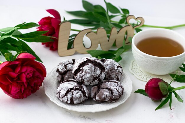 Leckereien auf einem weißen Tisch Chocolate Cracks Cookies eine Tasse Tee und Pfingstrosen