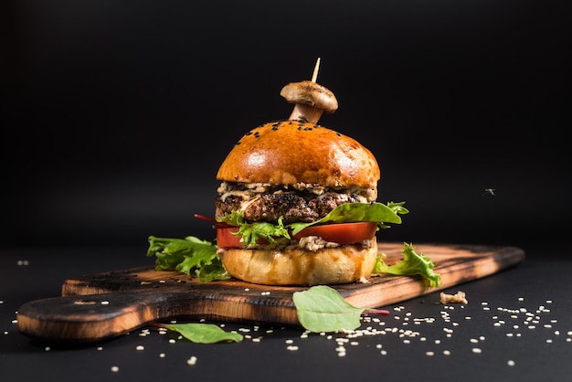 Leckerer Burger mit gegrilltem Fleisch und Pilzen auf schwarzem Hintergrund