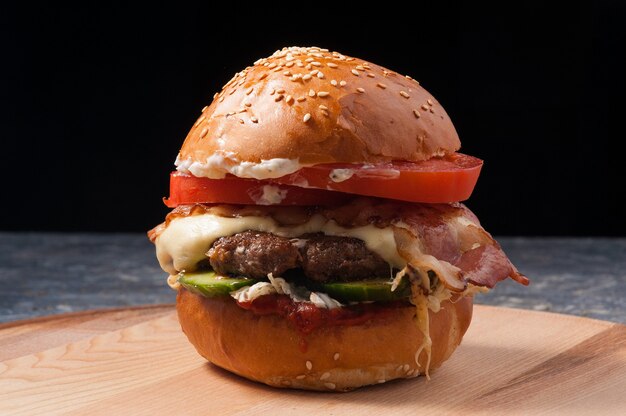 Leckerer Burger mit Rindfleisch, Käse, Speck und frischem Gemüse auf einem schwarzen Hintergrund