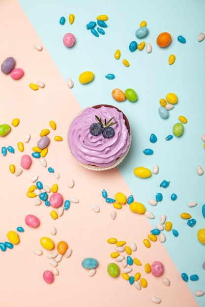 Leckerer Cupcake in der Nähe von süßen Süßigkeiten auf Pfirsich und blauem Hintergrund