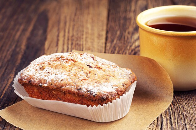 Leckerer Cupcake und heiße Tasse Tee auf Holztisch