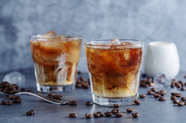 Leckerer erfrischender Eiskaffee mit Eiswürfeln in Gläsern auf hellem Hintergrund. Nahaufnahme