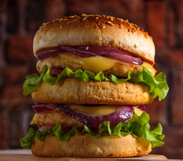 Leckerer gegrillter Burger mit Salat, Käse und Zwiebeln, serviert auf einem Schneidebrett auf einem Holztisch