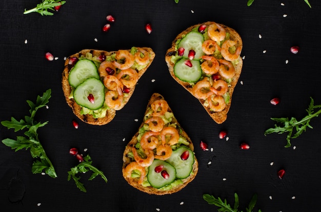 Leckerer, gesunder Snack mit Avocado-Toast, Gurke und Garnelen. Flachgelegt, Draufsicht.