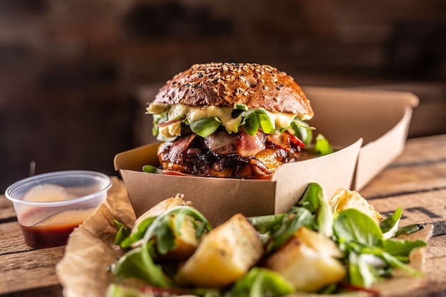 Leckerer hausgemachter Burger zum Mitnehmen in einer Schachtel aus Recyclingpapier auf Holzbrettern