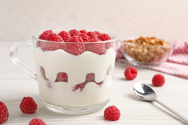 Leckerer Joghurt serviert mit Himbeeren und Müsli auf weißem Holztisch