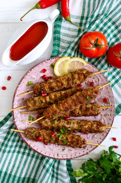 Leckerer Lula-Kebab auf dem Teller auf einem weißen Holztisch. Gehacktes Fleisch auf Holzspießen, gegrillt.