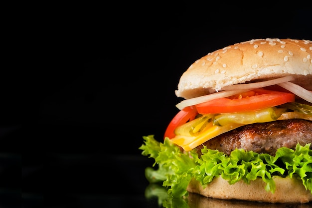 Leckerer Rindfleischburger mit Käsezwiebeltomate und Salat isoliert auf schwarzem Kopierplatz