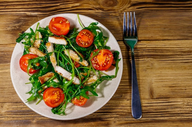 Leckerer Salat aus gebratener Hähnchenbrust, frischem Rucola und Kirschtomaten auf Holztisch Draufsicht