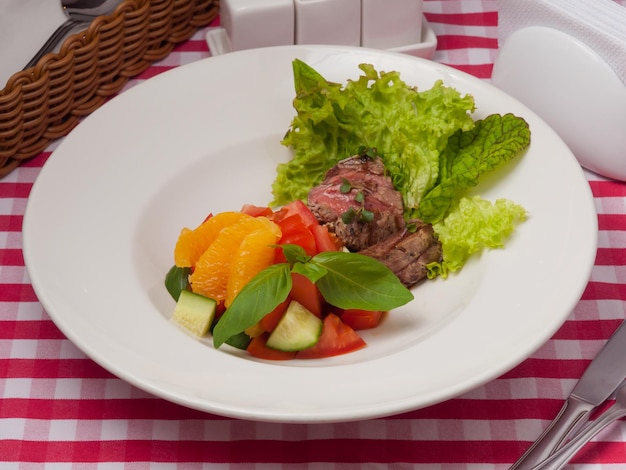 Leckerer Salat mit Gemüse, Rindfleisch und Orange auf einem weißen Teller