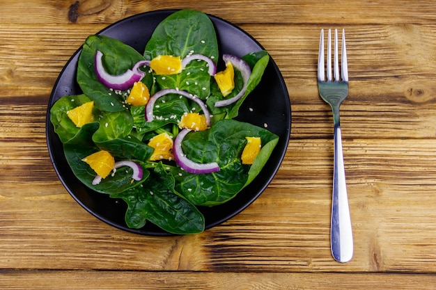 Leckerer Salat mit Spinat, orange, roter Zwiebel und Sesamsamen auf Holztisch Draufsicht Gesundes Essen oder vegetarisches Konzept