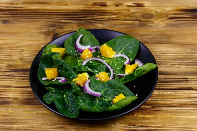 Leckerer Salat mit Spinat, orange, roter Zwiebel und Sesamsamen auf Holztisch Gesundes Essen oder vegetarisches Konzept