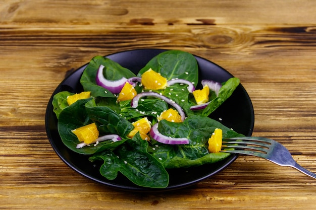 Foto leckerer salat mit spinat, orangeroten zwiebeln und sesam auf holztisch. gesunde ernährung oder vegetarisches konzept